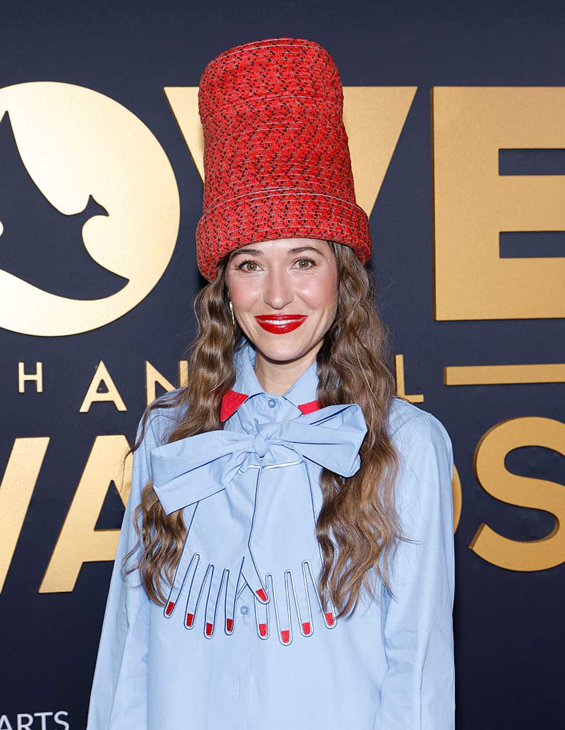 Lauren Daigle in a tall red knitted hat and a light-blue bow blouse, smiling at the camera at the 57th Annual Dove Awards at Bridgestone Arena in Nashville, 2026
