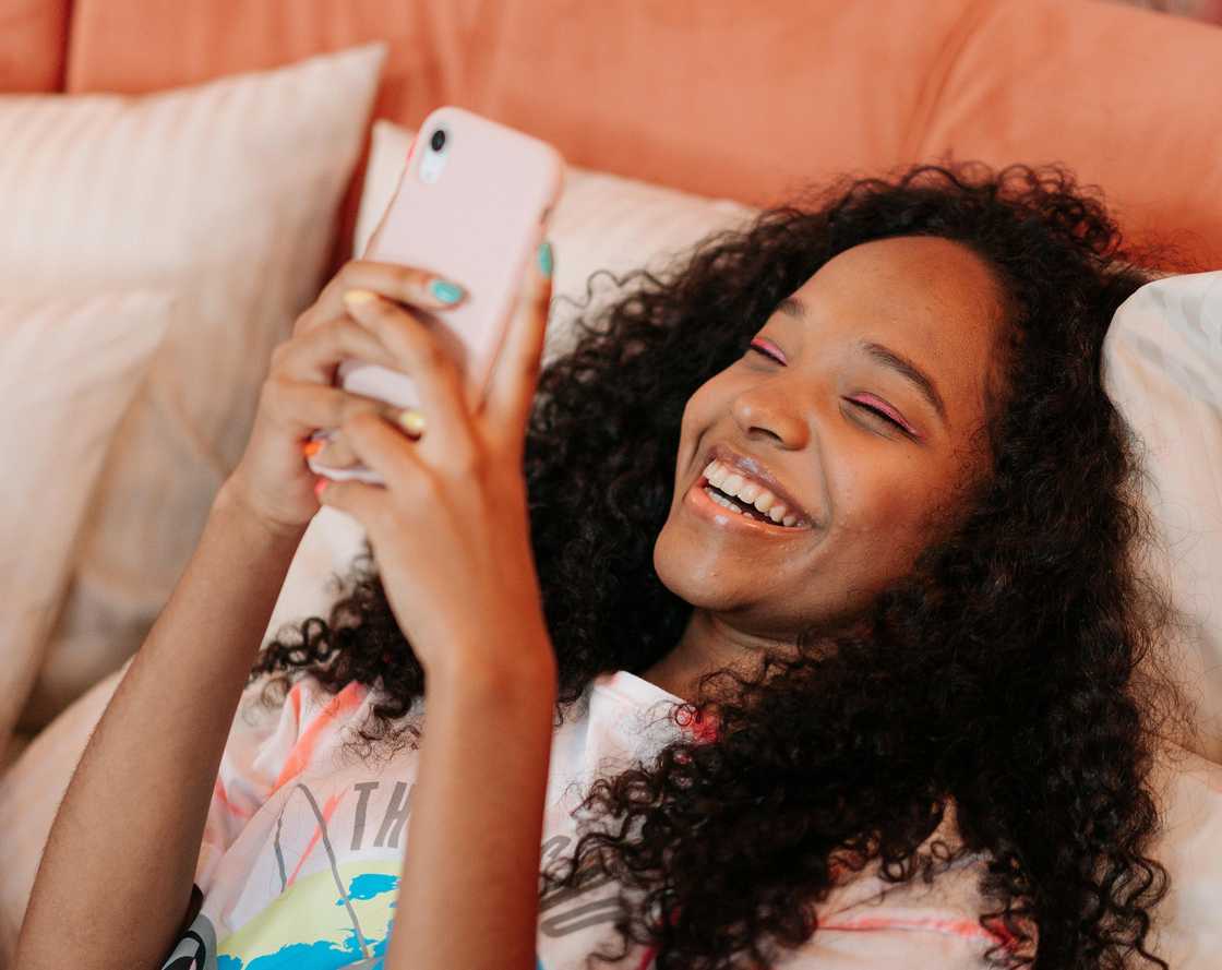 A teenage girl laughing with a smartphone on the bed A teenage girl laughing with a smartphone on the bed