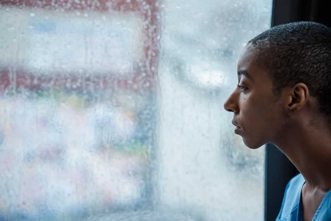 A woman looks out through a rain-covered window with a distant expression.