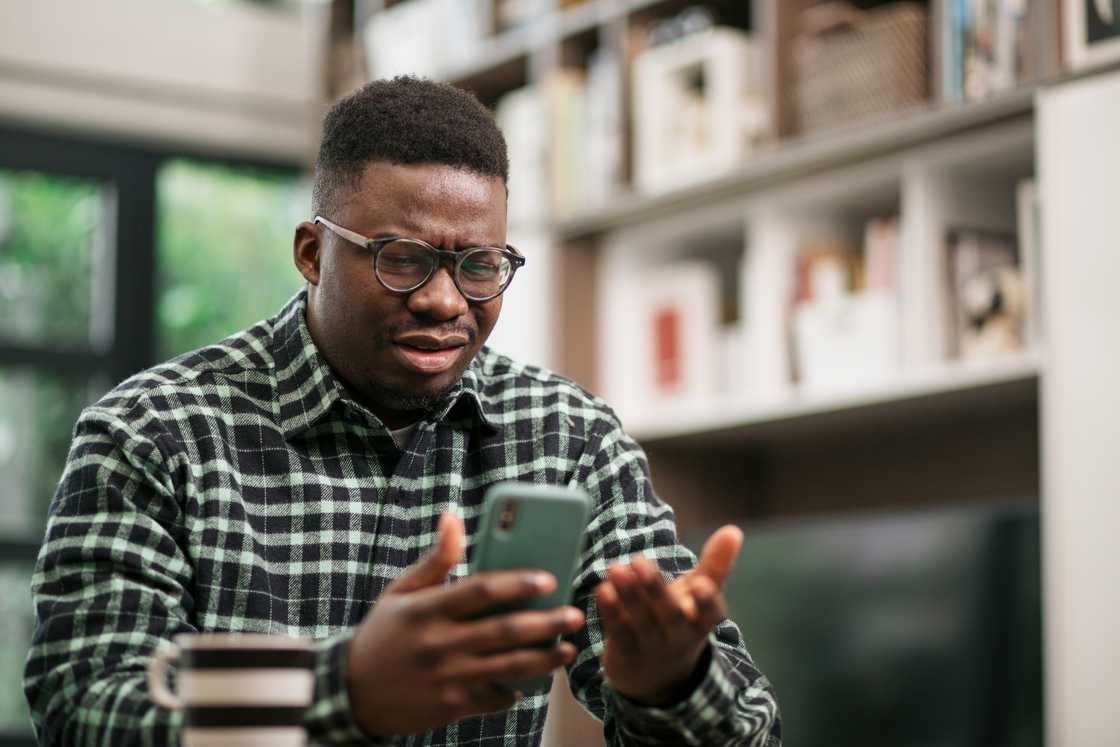 An annoyed young man sitting at home expressing his displeasure while checking his phone