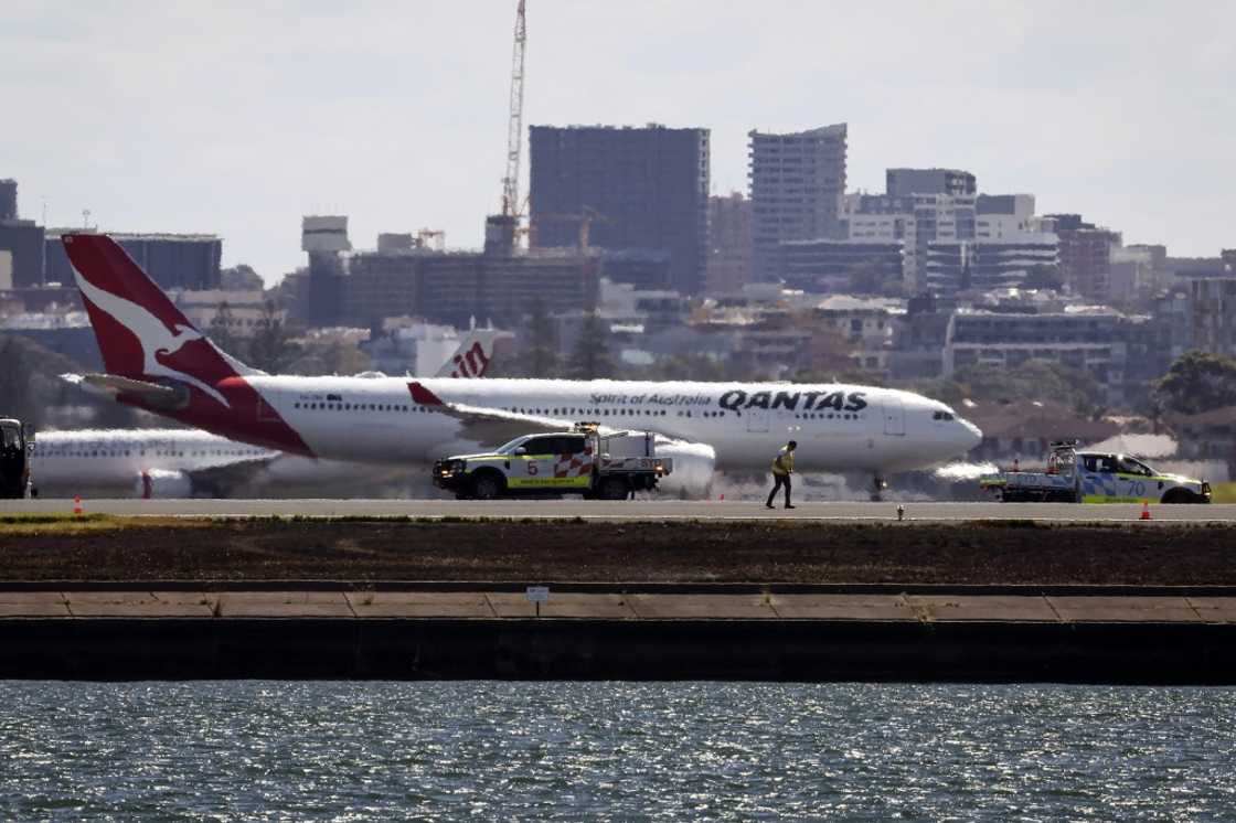 Workers check the runway as a Qantas plane prepares to take off behind them at Sydney Airport