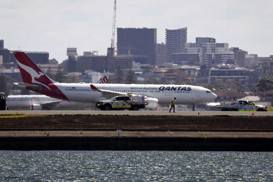 Workers check the runway as a Qantas plane prepares to take off behind them at Sydney Airport Workers check the runway as a Qantas plane prepares to take off behind them at Sydney Airport