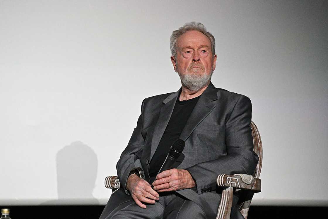 Ridley Scott seated in a chair on stage, holding a microphone.