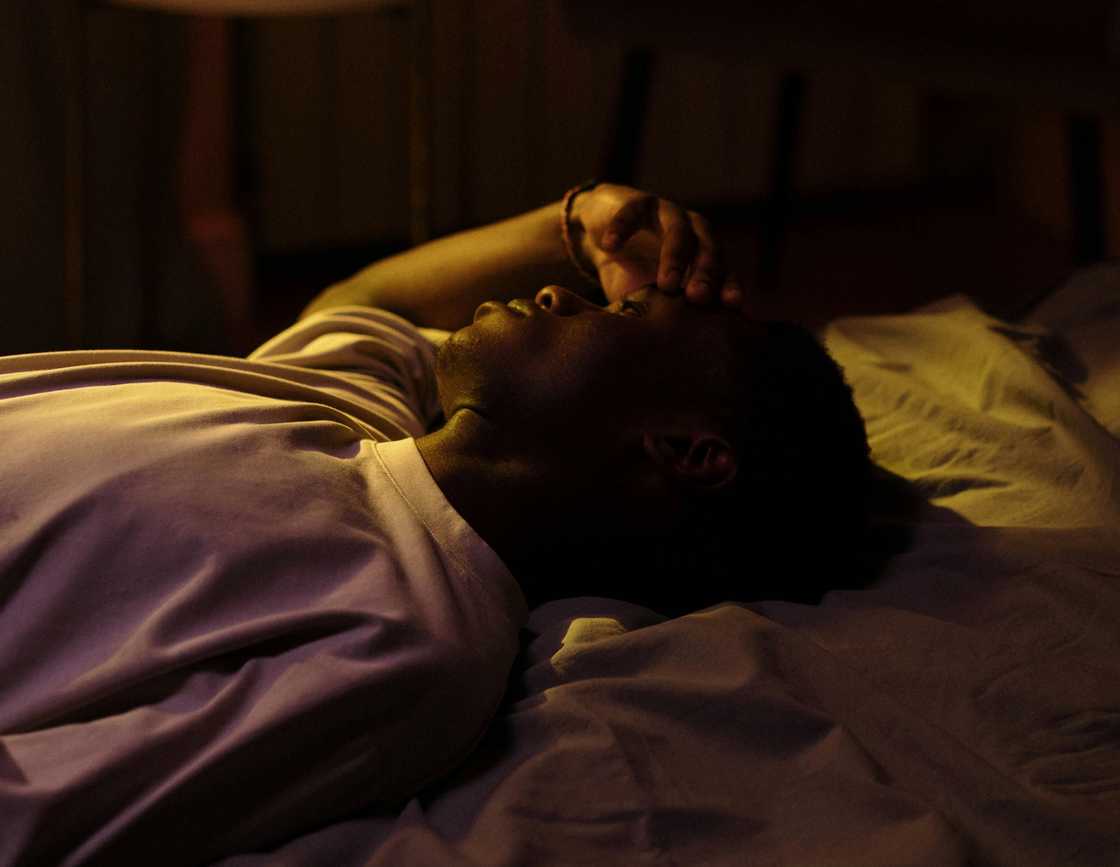 A man lying awake in bed at night, hand covering his face in grief. A man lying awake in bed at night, hand covering his face in grief.