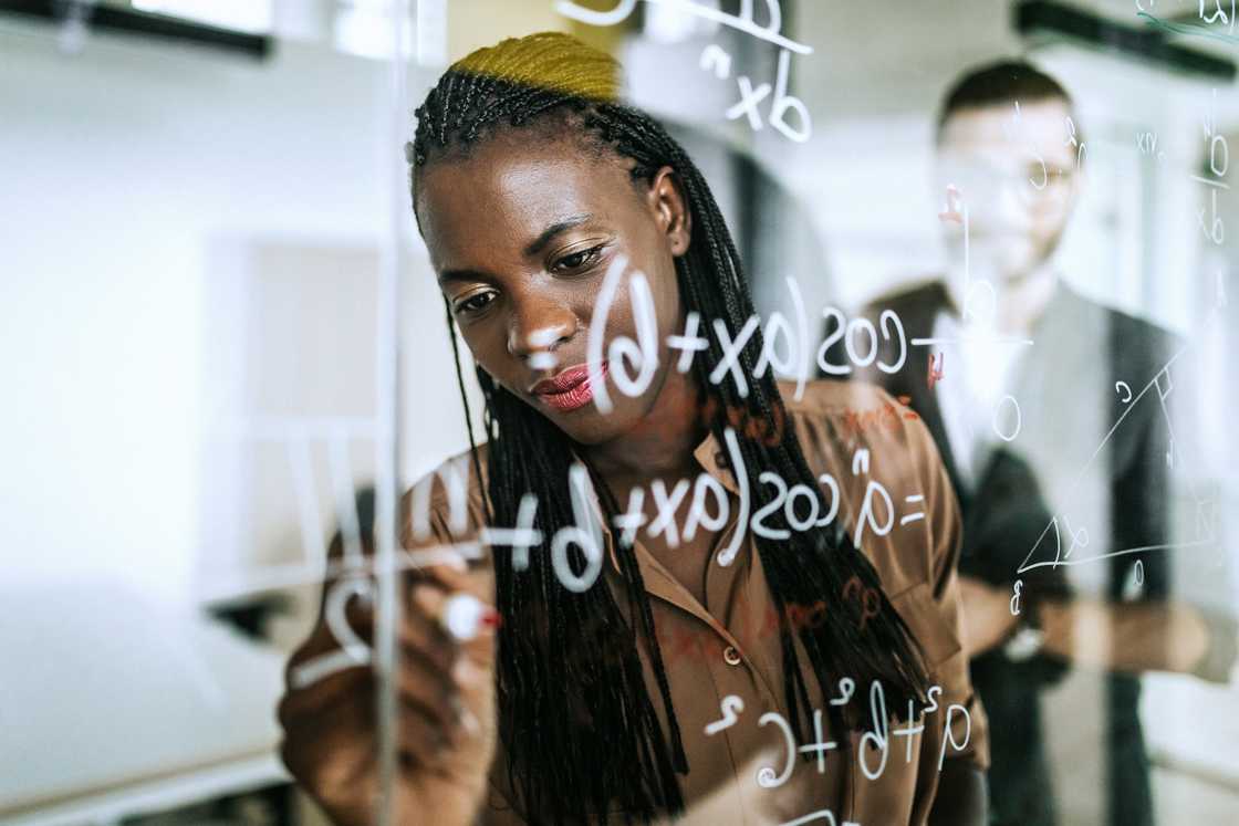 Colleagues writing mathematical formulas on transparent wipe board Colleagues writing mathematical formulas on transparent wipe board