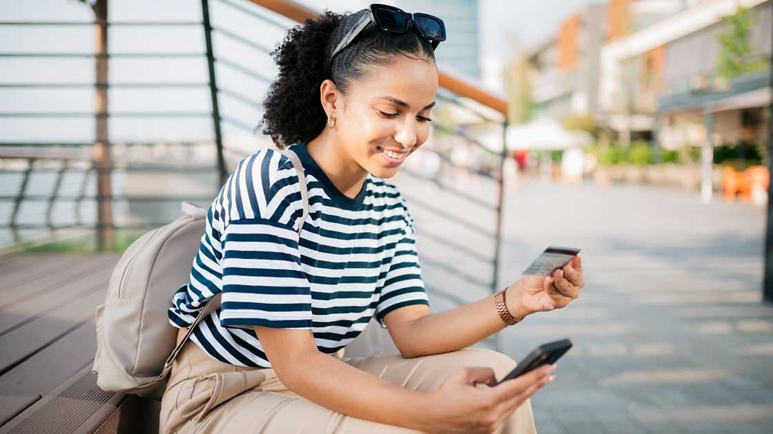 A woman is pictured sitted, checking her credit card and phone. A woman is pictured sitted, checking her credit card and phone.