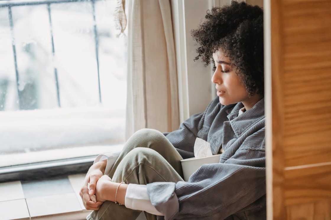 Sad woman sitting by a window holding a box of tissues. Sad woman sitting by a window holding a box of tissues.