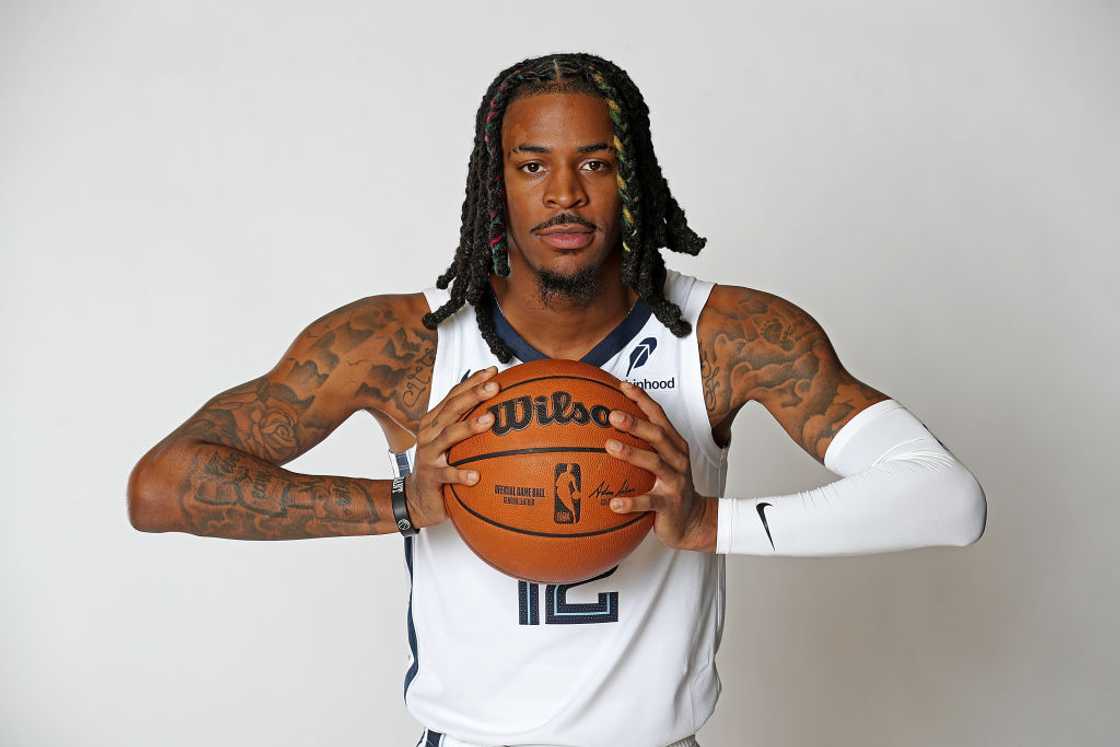 Ja Morant in a white Memphis Grizzlies No. 12 jersey holding a basketball in both hands and looking at the camera during media day at FedExForum, 2024 Ja Morant in a white Memphis Grizzlies No. 12 jersey holding a basketball in both hands and looking at the camera during media day at FedExForum, 2024