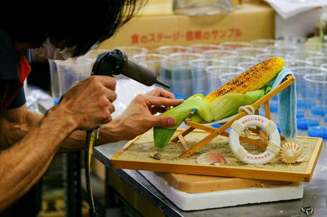 A worker applies the finishing touches to a plastic ear of grilled corn reclining on a beach chair A worker applies the finishing touches to a plastic ear of grilled corn reclining on a beach chair