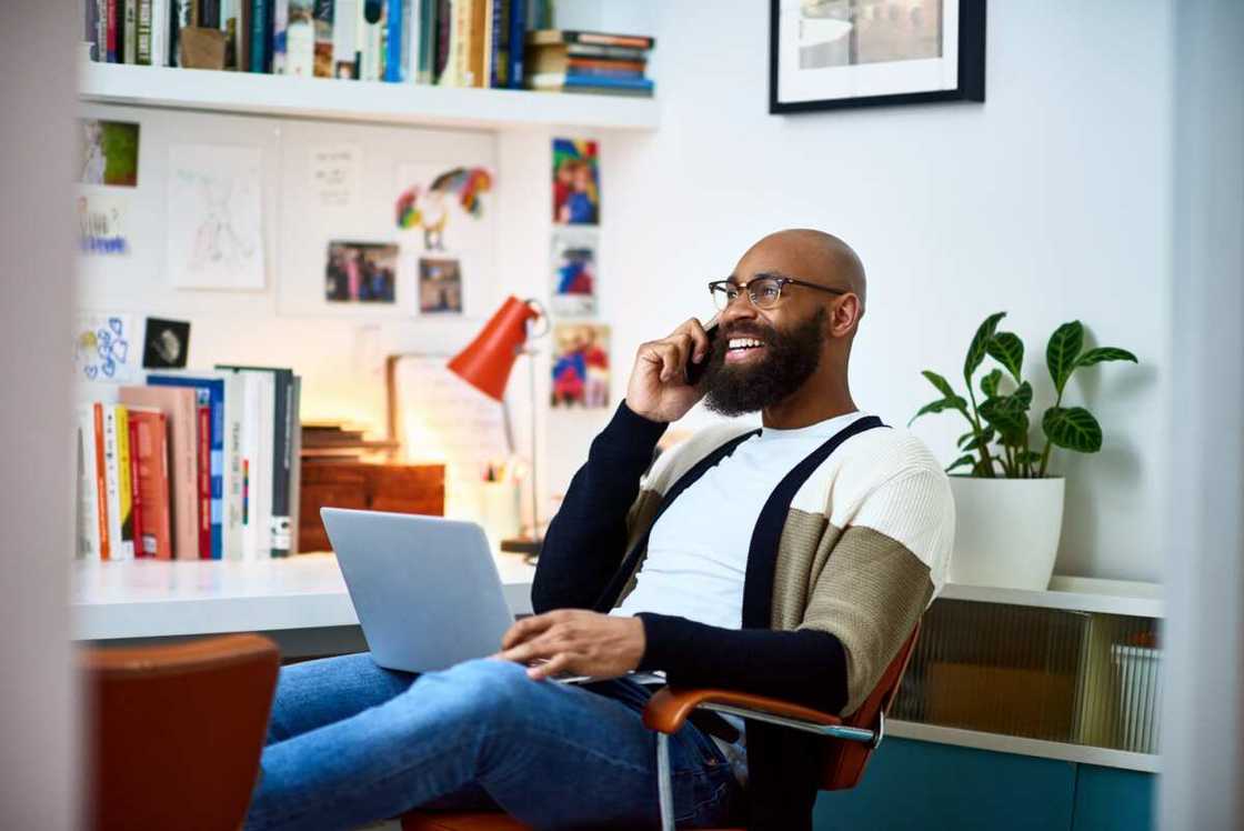 A man sitting on a chair with a laptop on a phone call