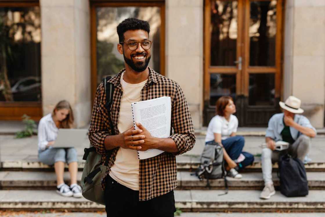Male student walking out from university, carrying a book Male student walking out from university, carrying a book