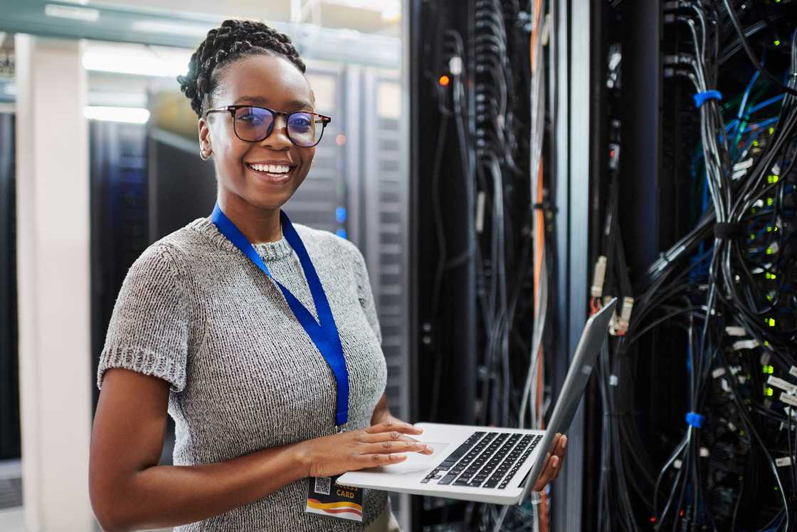 Portrait of a young woman using a laptop in a server room.