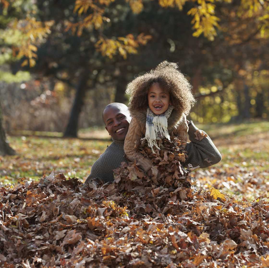 A father and daughter playing in pile of autumn leaves