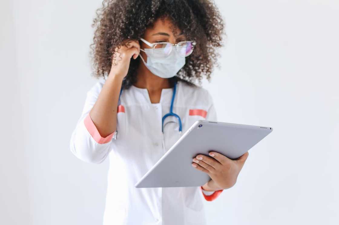 A female healthcare worker wearing a mask and reading a tablet. A female healthcare worker wearing a mask and reading a tablet.