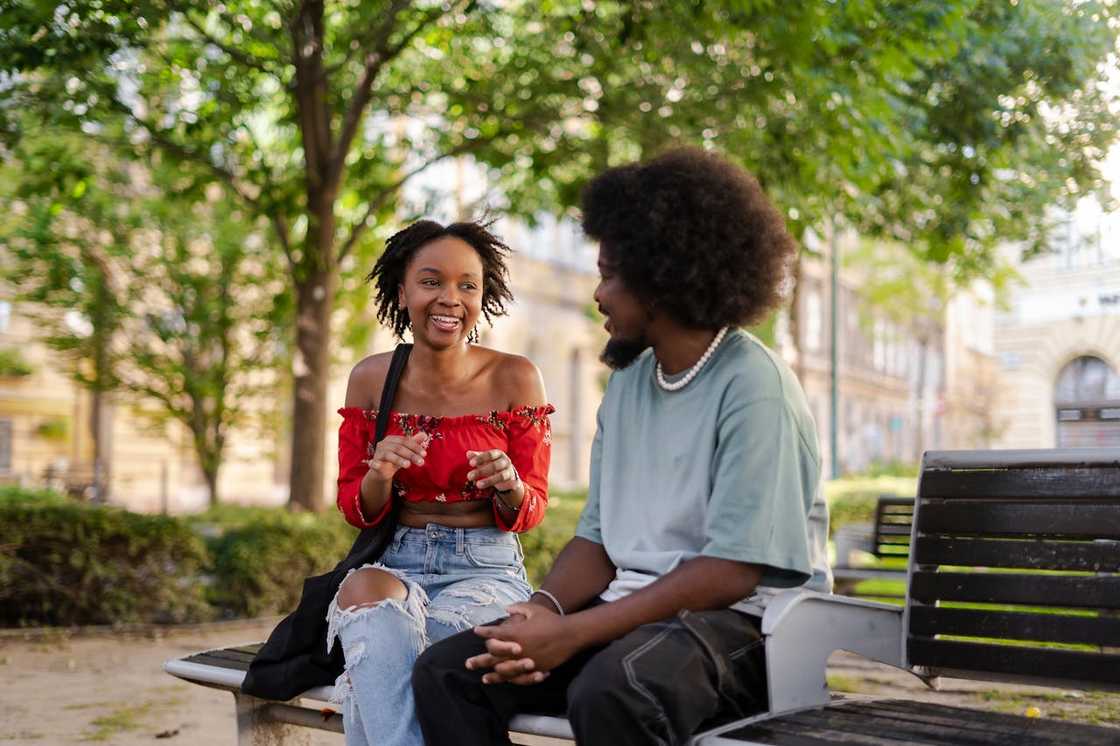 A young couple smiling and talking on a park bench.