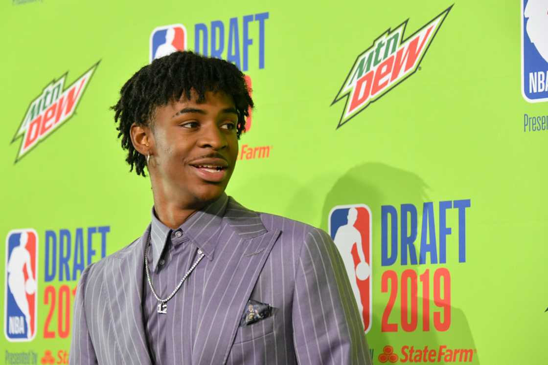 A smiling Ja Morant in a lavender pinstripe suit in front of a green 2019 NBA Draft backdrop at Barclays Center in New York A smiling Ja Morant in a lavender pinstripe suit in front of a green 2019 NBA Draft backdrop at Barclays Center in New York