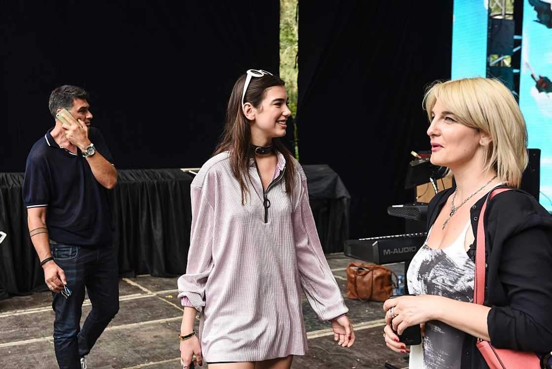 A woman in an oversized pink shirt dress with sunglasses on her head talks to another woman. A woman in an oversized pink shirt dress with sunglasses on her head talks to another woman.