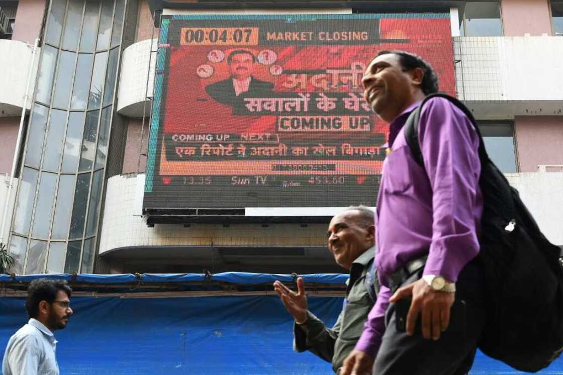 Pedestrians walk past a screen displaying news on the Adani Group at the Bombay Stock Exchange Pedestrians walk past a screen displaying news on the Adani Group at the Bombay Stock Exchange