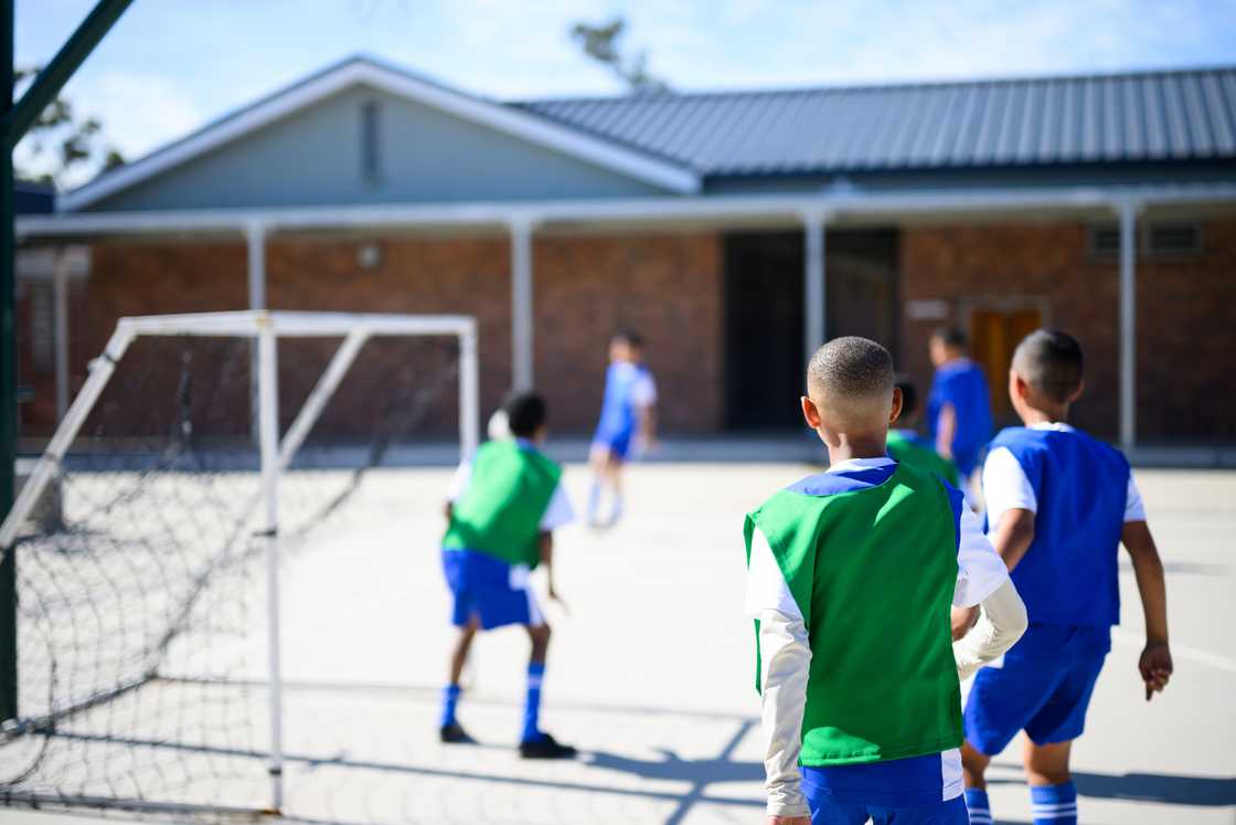 Children play soccer on a school court, with one defending the goal. Children play soccer on a school court, with one defending the goal.