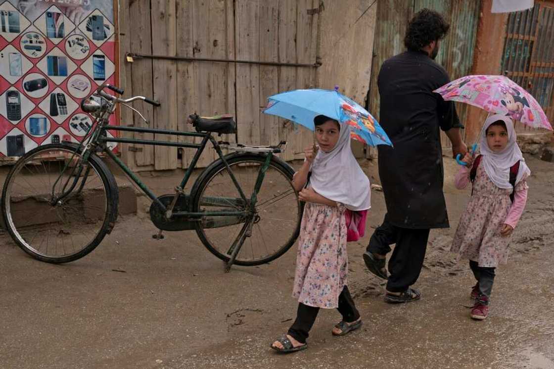 Afghan girls hold umbrellas as they walk along a street in Parwan province on August 25, 2022 Afghan girls hold umbrellas as they walk along a street in Parwan province on August 25, 2022