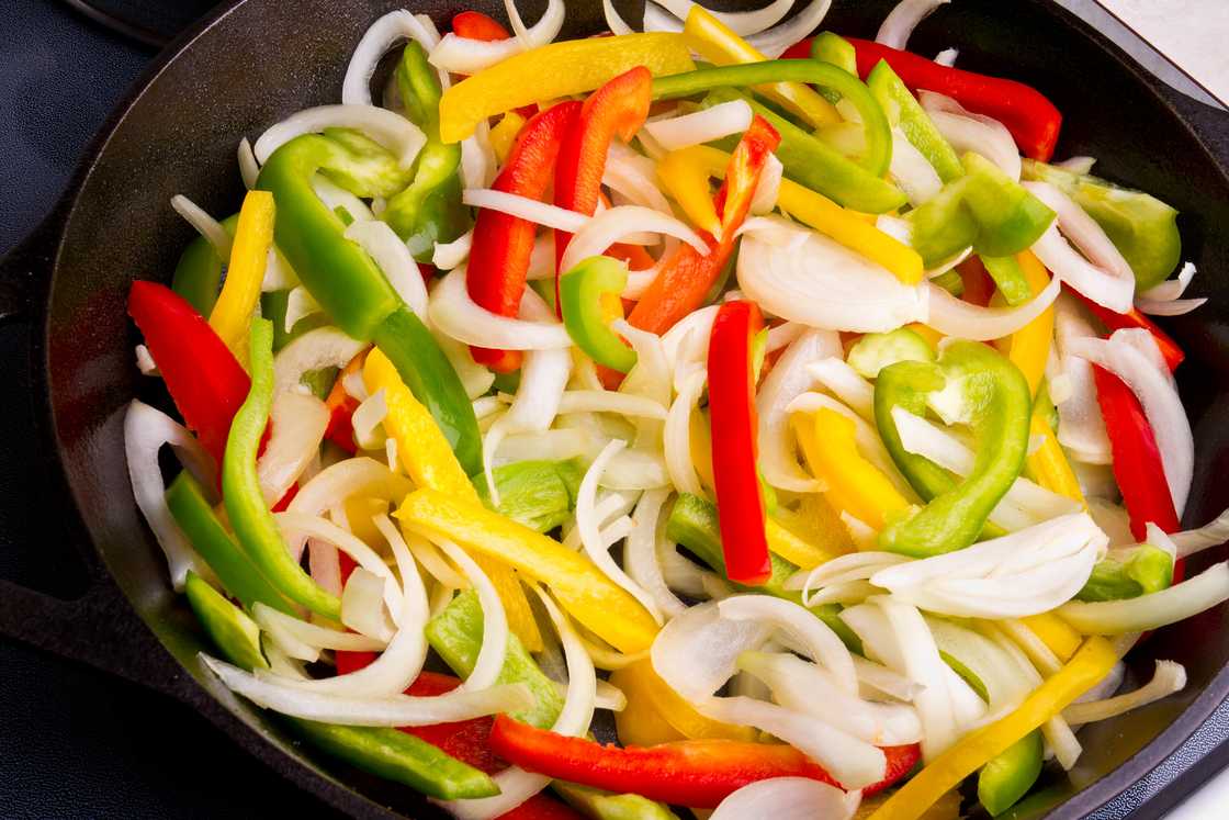 Sliced green, red and yellow bell peppers in a pan being sautéed in olive oil and spices Sliced green, red and yellow bell peppers in a pan being sautéed in olive oil and spices