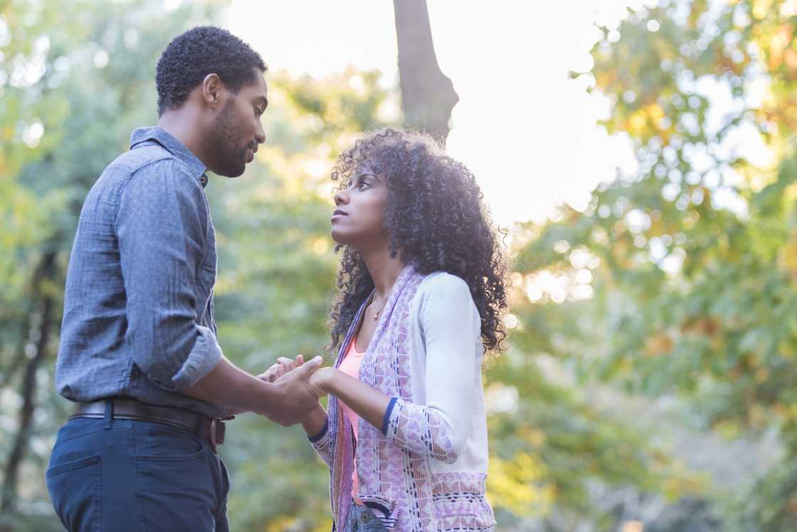 A young couple stands outside in the sunlight holding hands A young couple stands outside in the sunlight holding hands