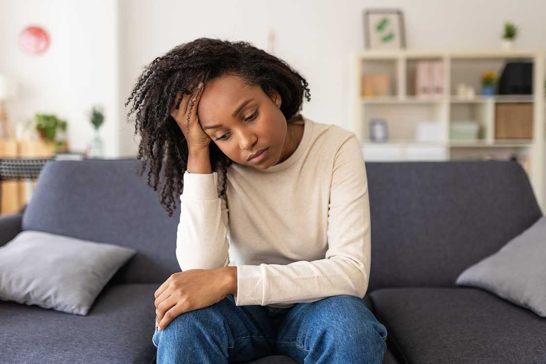 A sad woman thinking about her problems while sitting alone on a sofa at home. A sad woman thinking about her problems while sitting alone on a sofa at home.
