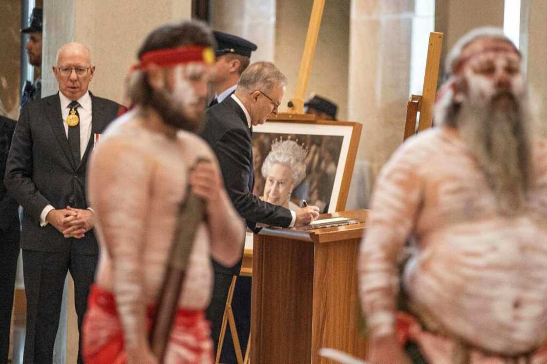 Australia's Prime Minister Anthony Albanese (C) writes in a book as Australia's Governor-General David Hurley (L) looks on during the national service for Britain's Queen Elizabeth II