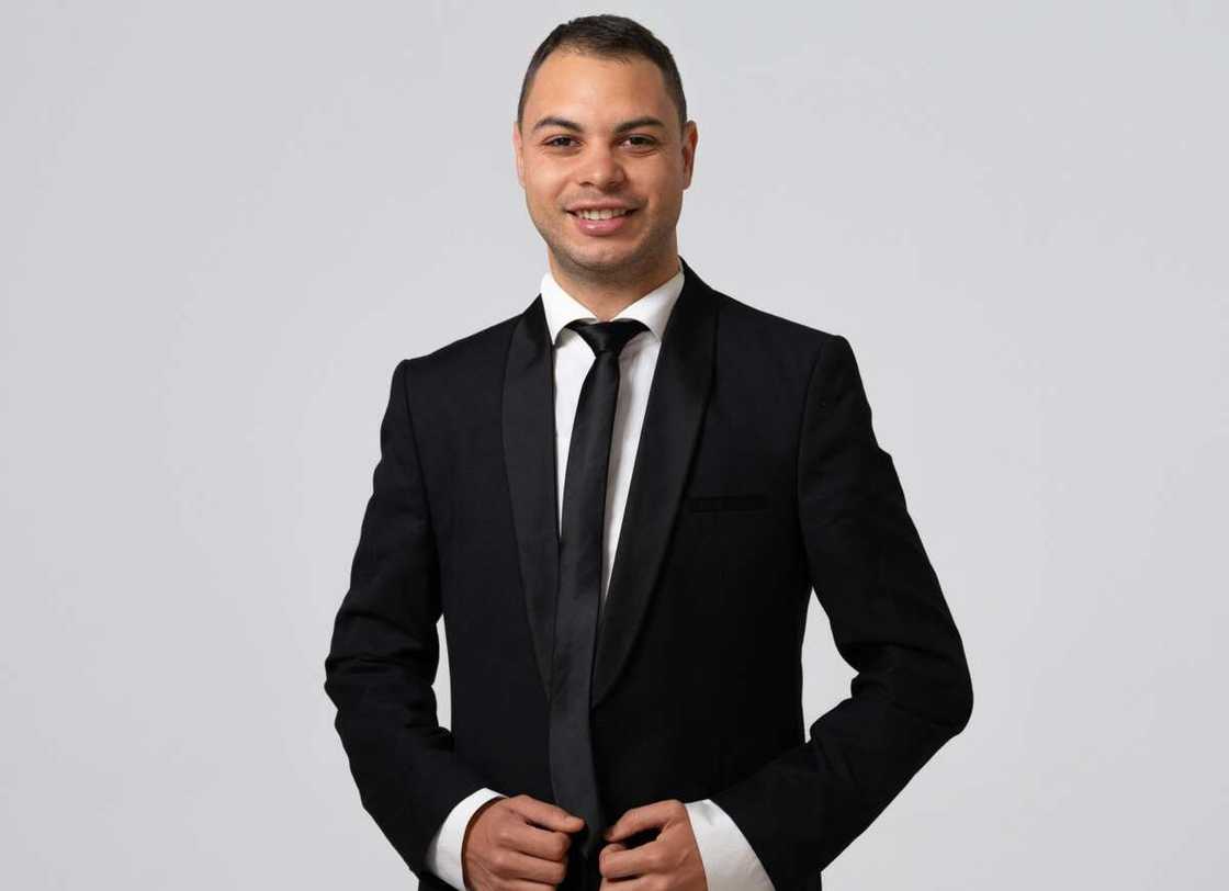 A man in a black suit and white shirt smiling