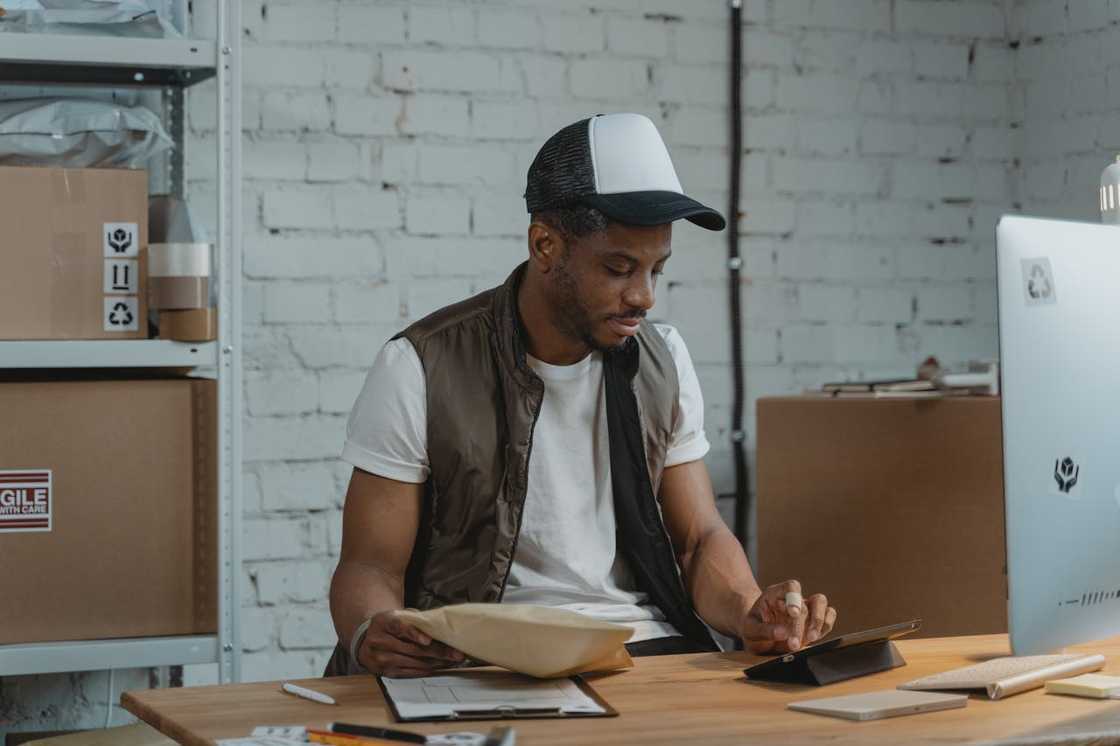 A warehouse worker seated at a desk, checking a package and using a tablet.