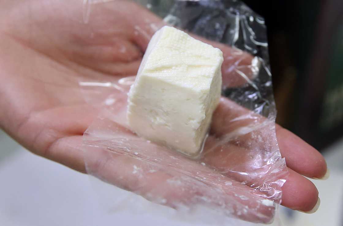 An employee displays a 50 gram block of pule cheese. An employee displays a 50 gram block of pule cheese.