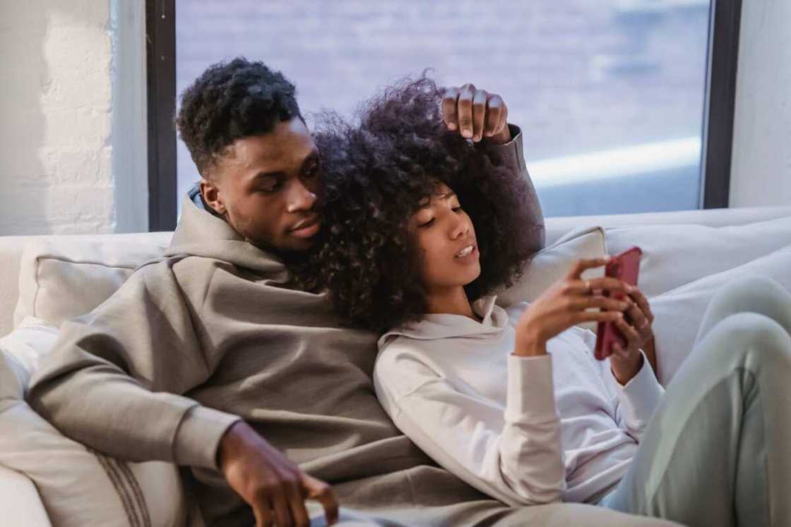 Young black woman resting together with boyfriend and using smartphone Young black woman resting together with boyfriend and using smartphone