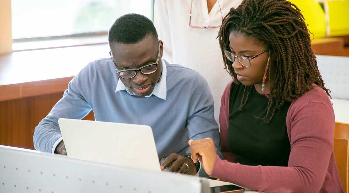 Two students are looking at a laptop in a classroom.