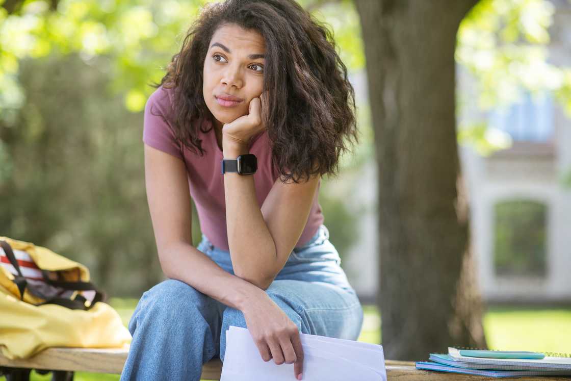A woman sitting outdoors holding a report card and looking reflective.