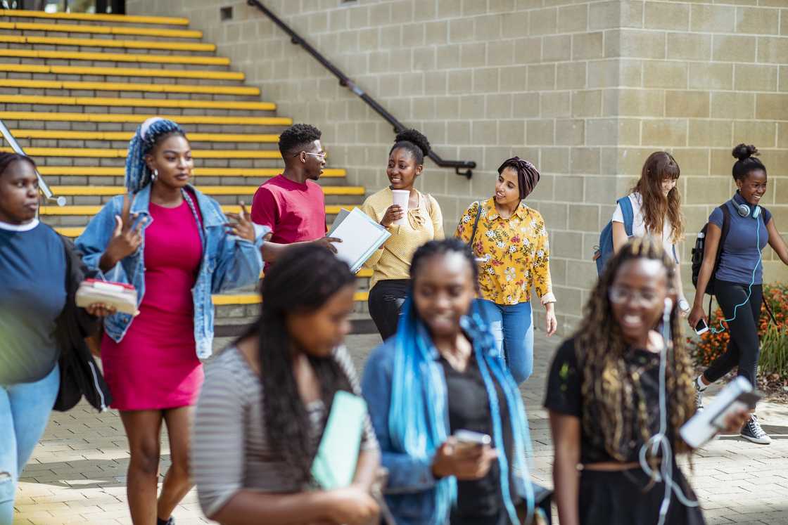 A diverse group of students in their 20's walking down some steps on campus laughing and talking to each other. A diverse group of students in their 20's walking down some steps on campus laughing and talking to each other.