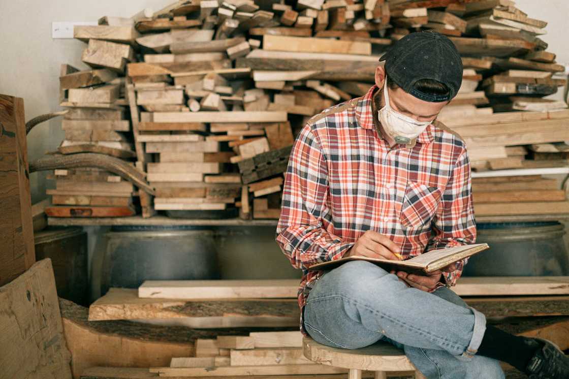 A worker wearing a mask writes notes in a timber workshop. A worker wearing a mask writes notes in a timber workshop.