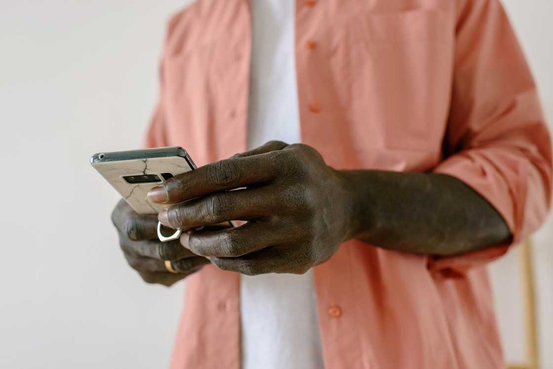 A man in a mauve shirt is using a smartphone