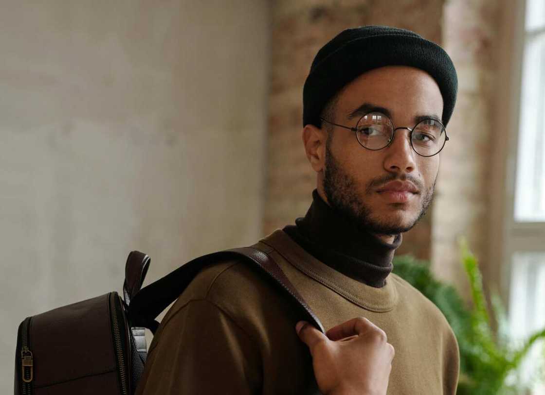 A man in a brown coat and a black cap carrying a backpack A man in a brown coat and a black cap carrying a backpack