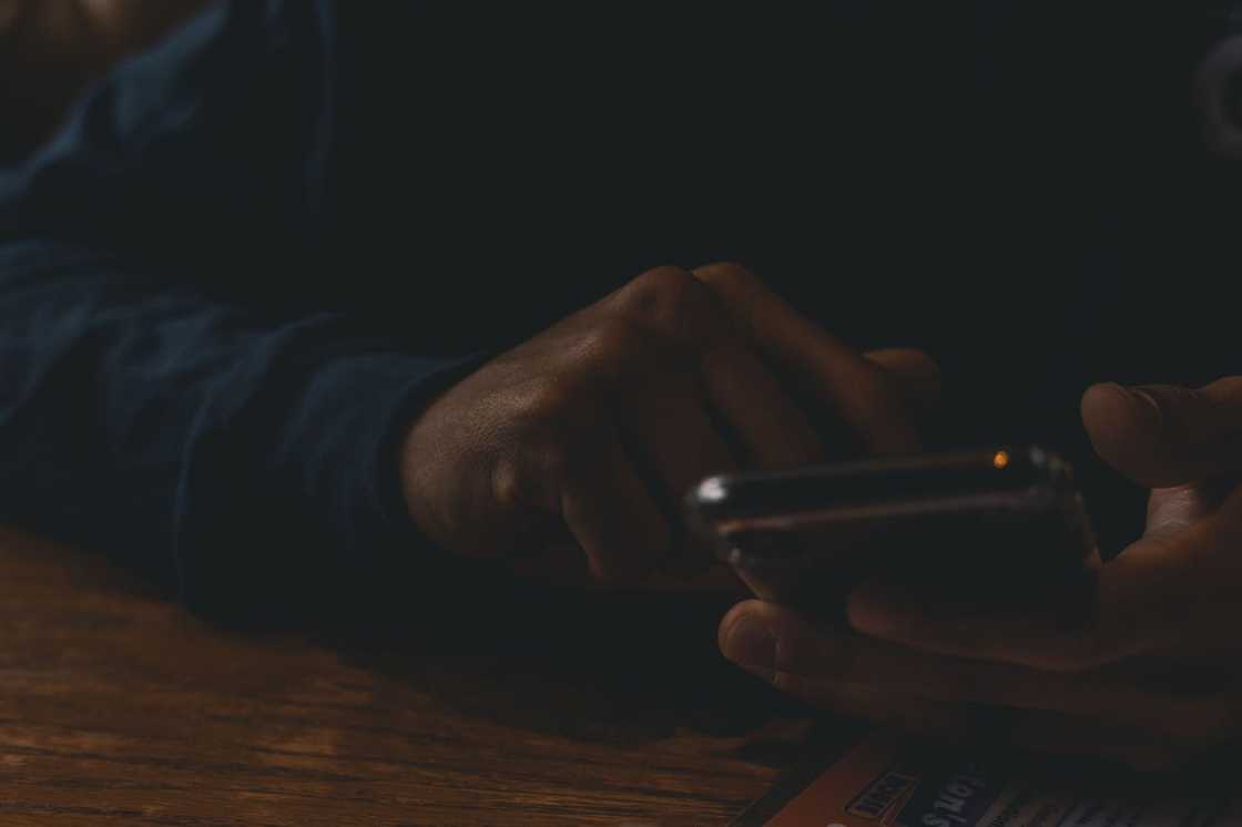 Hands hold a phone in low light.