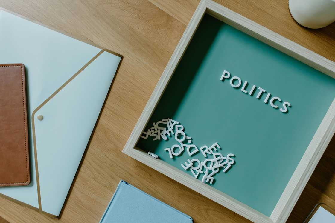 A blue and white box with the word politics beside a white envelope on a wooden surface A blue and white box with the word politics beside a white envelope on a wooden surface