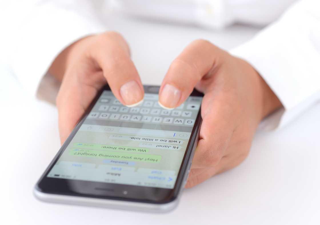 Hands holding a phone displaying WhatsApp messaging application.