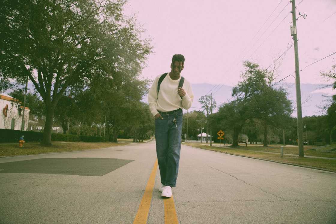 A young man walks alone toward a bus stop in early morning light.