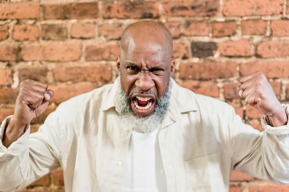 An angry man shouting with fists raised in front of a brick wall. An angry man shouting with fists raised in front of a brick wall.
