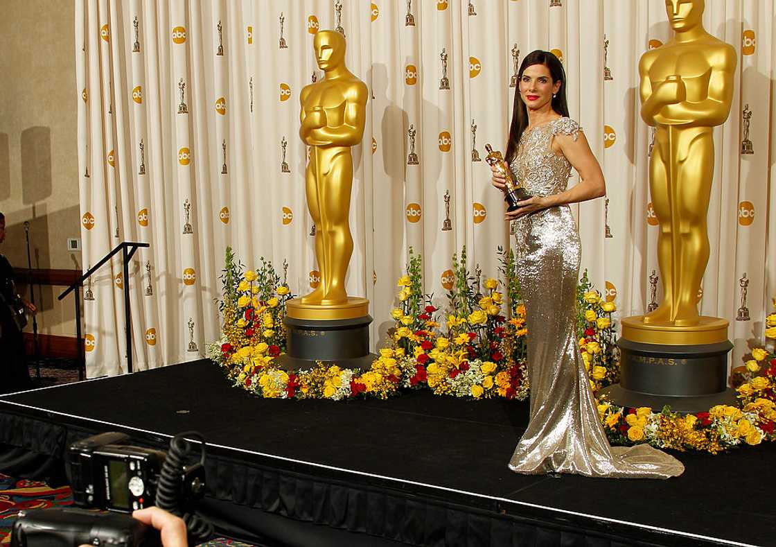 Sandra Bullock in a silver beaded gown holding her Academy Award between two golden Oscar statues in the press room in Hollywood, 2010 Sandra Bullock in a silver beaded gown holding her Academy Award between two golden Oscar statues in the press room in Hollywood, 2010