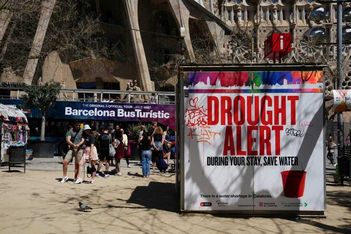 A couple uses a selfie stick to take a picture next to a banner warning tourists about a drought alert in Catalonia
