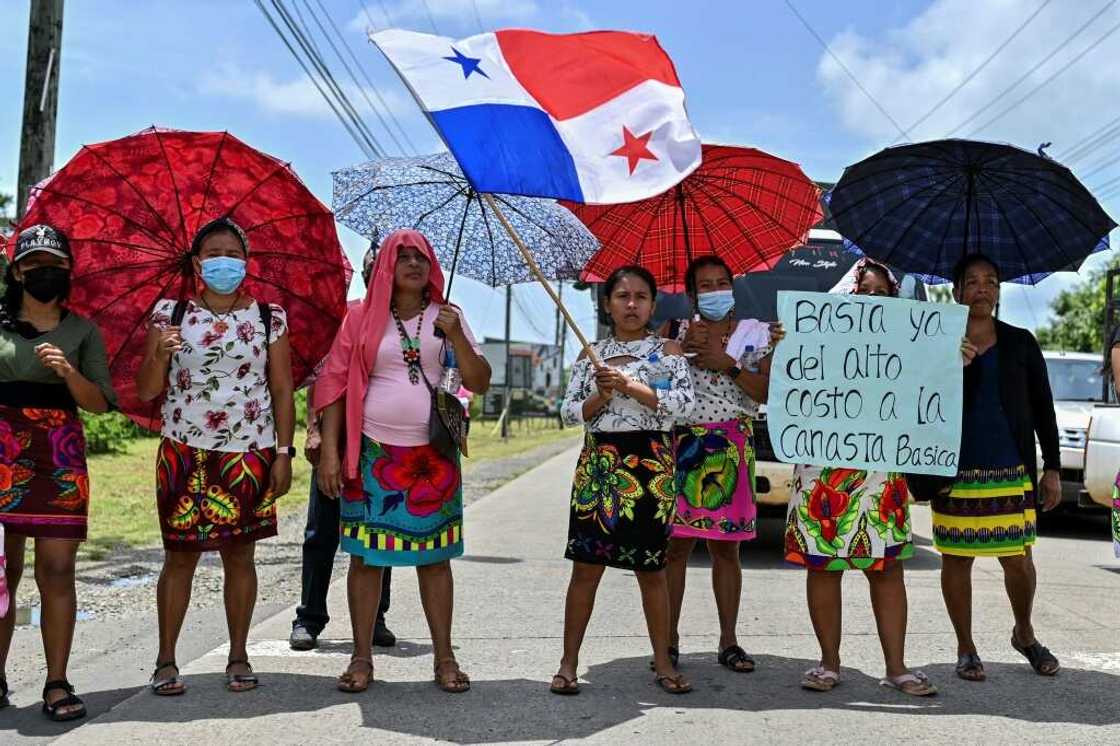 Embera indigenous women with umbrellas and a Panamanian flag block the Pan-American highway during a protest against fuel prices on July 20, 2022 Embera indigenous women with umbrellas and a Panamanian flag block the Pan-American highway during a protest against fuel prices on July 20, 2022
