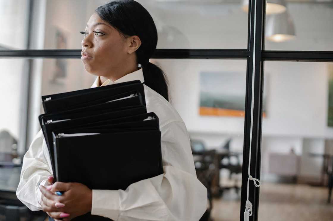 A woman holds several black folders in a modern workspace. A woman holds several black folders in a modern workspace.
