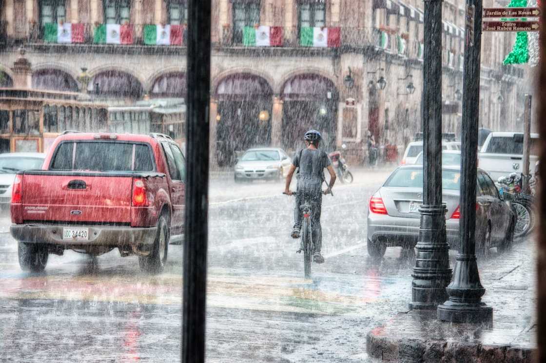 A cyclist riding through heavy rain on a busy city street. A cyclist riding through heavy rain on a busy city street.