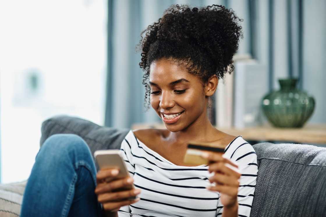 A young woman using her credit card while browsing on her cellphone A young woman using her credit card while browsing on her cellphone