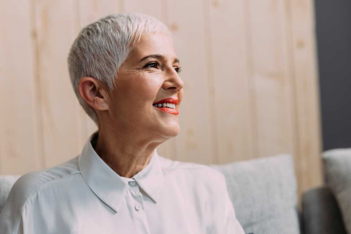 A senior woman with a short crop haircut poses while sitting.